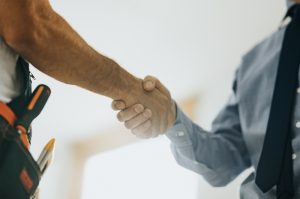 worker-with-tool-belt-and-homeowner-with-shirt-and-tie-shaking-hands